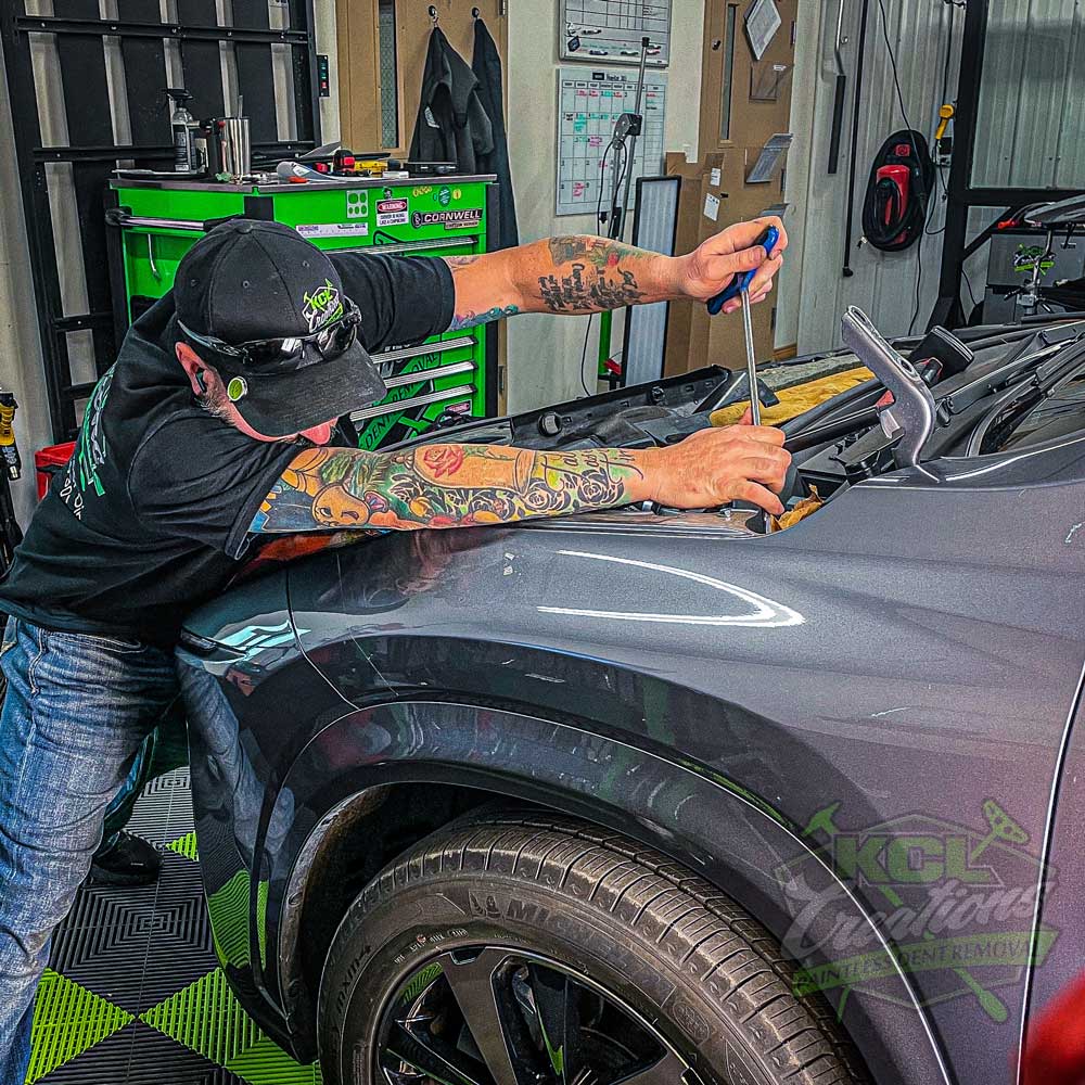 KCL Creations technician performing paintless dent repair on a vehicle panel in the shop